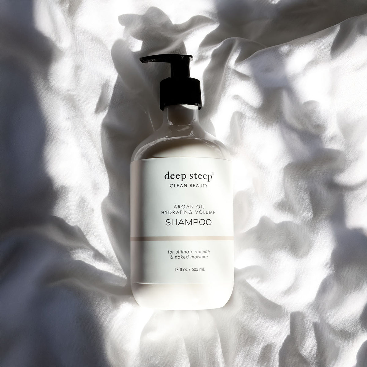 Bottle of Deep Steep Argan Oil Hydrating Volume Shampoo on a textured white fabric background
