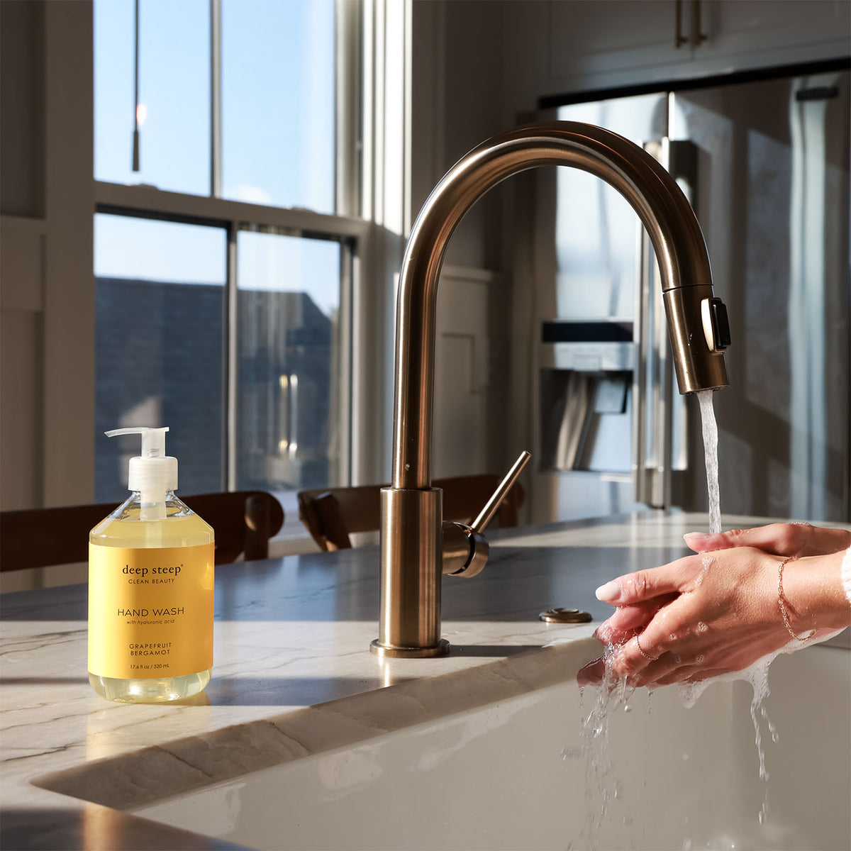 Person washing hands with soap under a running faucet, next to a bottle of Deep Steep Grapefruit Bergamot Liquid Hand Wash, 17.6 fl oz bottle on a countertop
