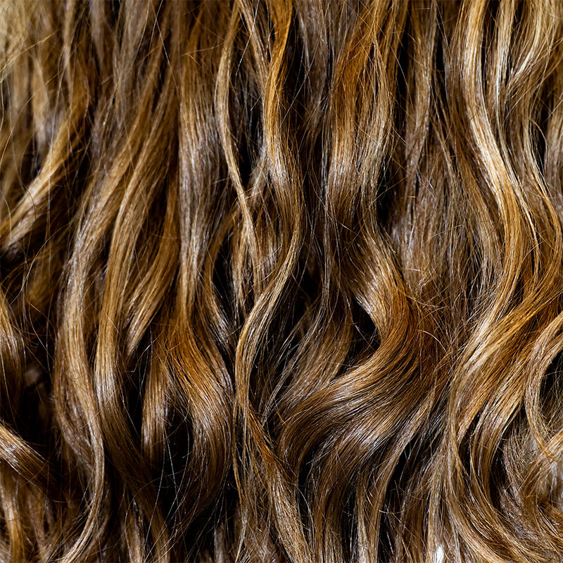 Close-up view of healthy, glossy brown and blonde highlighted wavy hair representing Deep Steep hair care collection.