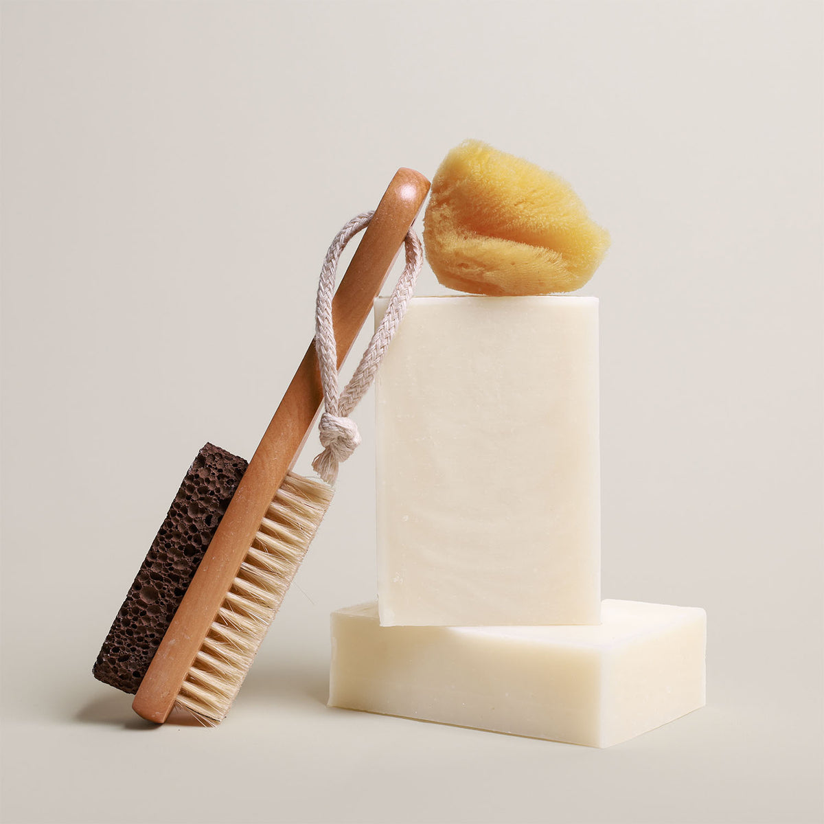 7 oz Deep Steep hydrating bar soap containing 40% shea butter stacked with a bath sponge and a wooden body brush on a neutral background
