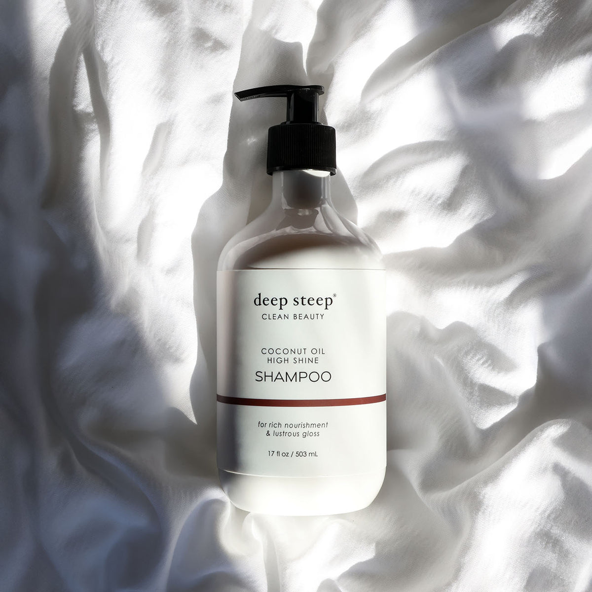 Bottle of Deep Steep Coconut Oil High Shine Shampoo on a textured white fabric background