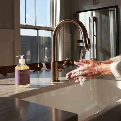 Person washing hands with soap under a running faucet, next to a bottle of Deep Steep Fig Apricot Liquid Hand Wash, 17.6 fl oz bottle on a countertop