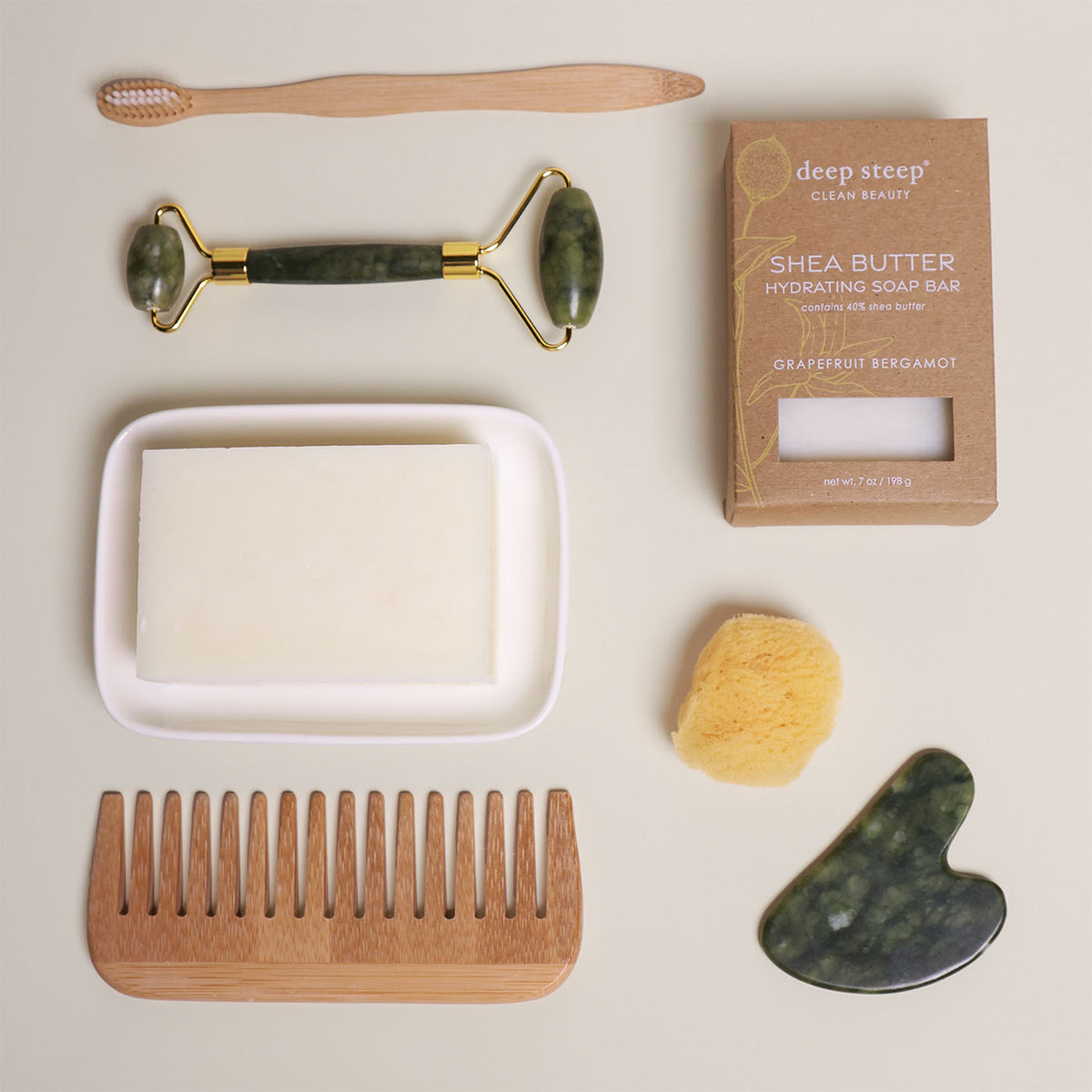 7 oz Deep Steep Grapefruit Bergamot hydrating bar soap containing 40% shea butter displayed with a soap dish, wooden comb, toothbrush, face roller, gua sha, and sponge on a neutral background