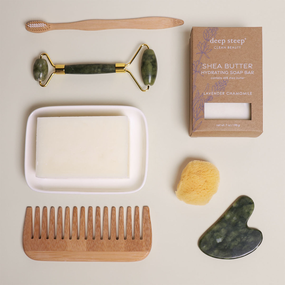 7 oz Deep Steep Lavender Chamomile hydrating bar soap containing 40% shea butter displayed with a soap dish, wooden comb, toothbrush, face roller, gua sha, and sponge on a neutral background