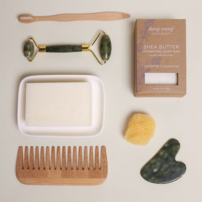 7 oz Deep Steep Lavender Chamomile hydrating bar soap containing 40% shea butter displayed with a soap dish, wooden comb, toothbrush, face roller, gua sha, and sponge on a neutral background