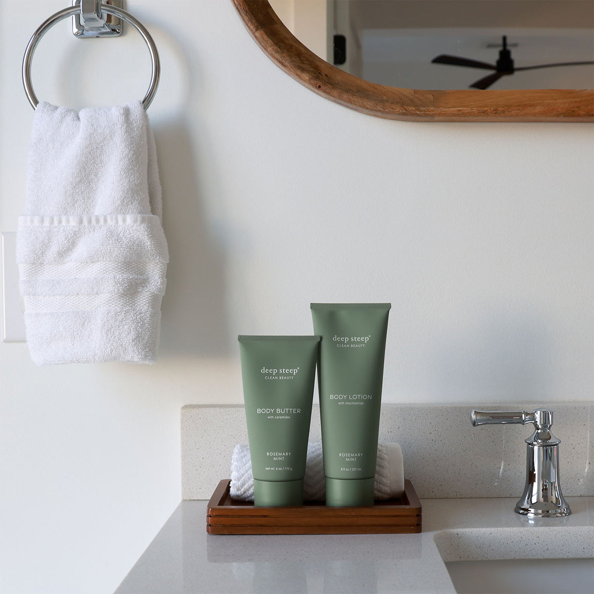 Two tubes of Deep Steep Rosemary Mint body lotion and body butter on a wooden tray on a bathroom counter