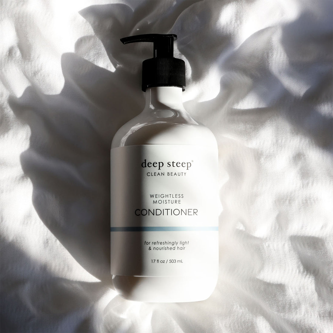 Bottle of Deep Steep Weightless Moisture Conditioner on a textured white fabric background