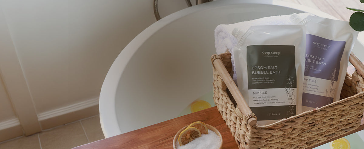 Two bags of Deep Sea Salt Bubble Bath in a woven basket next to a white bathtub on a wooden ledge.